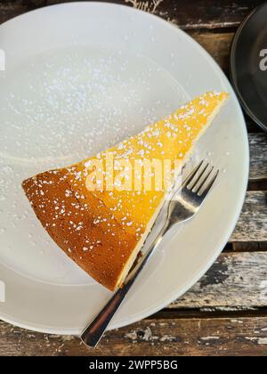 Ein Stück Käsekuchen mit Puderzucker auf einem weißen Teller zum Nachtisch Stockfoto