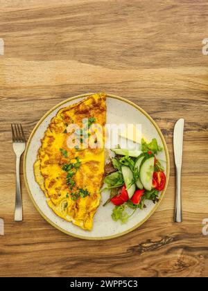 Herzhaftes Omelette mit Petersilie auf einem Teller mit Gurke, Tomatenscheiben, Salat, Butter Stockfoto