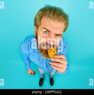 Bärtiger Mann isst Haferflockenkekse. Gutaussehender Mann mit Bart, der leckere Schokoladenkekse isst. Frühstück oder Mittagessen. Bäckerei. Rezept hausgemacht Stockfoto