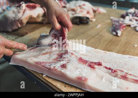 Nahaufnahme der Hände eines Metzgers, der rohe Fleischscheiben von einer großen Lende schneidet. Hochwertige Fotos Stockfoto