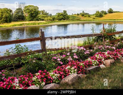 Wunderschöne Reihe von Begonien und Blumen entlang eines geteilten Bahnzauns neben einem wunderschönen Teich im Landkreis bei Panola Valley Gardens, einem Veranstaltungsort für Hochzeiten. Stockfoto