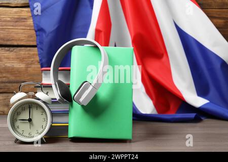 Fremdsprachenlernen. Verschiedene Bücher, Kopfhörer und Wecker auf Holztisch in der Nähe der Flagge von Großbritannien, Platz für Text Stockfoto