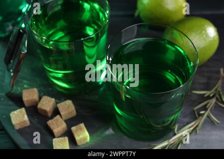 Absinth in Gläsern, Rosmarin, brauner Zucker und Limette auf dem Tisch, Nahaufnahme. Alkoholisches Getränk Stockfoto