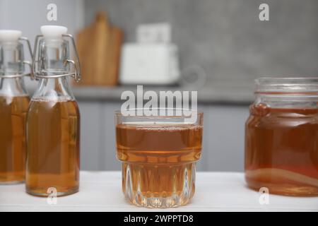 Hausgemachte fermentierte Kombucha in Glas, Glas und Flaschen auf weißem Tisch in der Küche Stockfoto