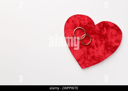 Flitterwochen-Konzept. Rotes Samtherz und zwei goldene Ringe auf weißem Hintergrund, Draufsicht. Leerzeichen für Text Stockfoto