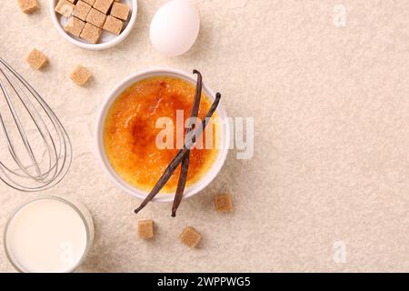 Köstliche Creme Brulee in der Schüssel und Zutaten auf leicht strukturiertem Tisch, flach gelegt. Leerzeichen für Text Stockfoto