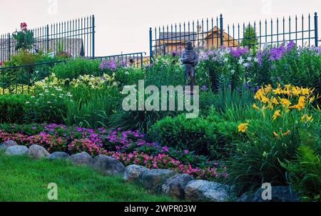 Statue von St. Francis von Assisi an einem Sommerabend in den Panola Valley Gardens, einem Veranstaltungsort für Hochzeiten, zwischen den wunderschönen blühenden Lilien und Pflanzen. Stockfoto