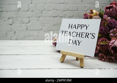 Text zum Happy Teachers Day auf weißer Ziegelwand und hölzernem Hintergrund Stockfoto