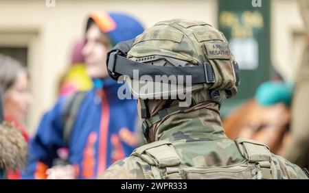 Ein Soldat, der eine normale Tarnhelm-Uniform und Kampfausrüstung trägt, wird von hinten gesehen und sieht sich einer bunten Menschenmenge im Kriegseinsatz, der nationalen Verteidigung A, gegenüber Stockfoto
