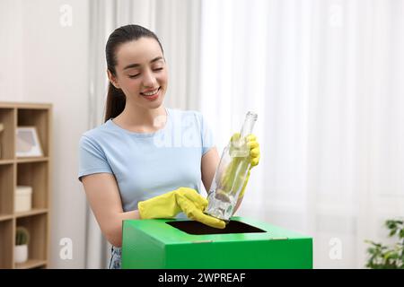 Müllsortierung. Lächelnde Frau, die Glasflasche in den Karton im Zimmer wirft Stockfoto