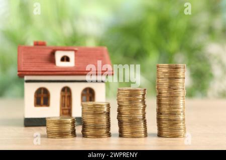 Hypothekenkonzept. Modellhaus und Münzstapel auf Holztisch vor verschwommenem grünem Hintergrund, Nahaufnahme Stockfoto