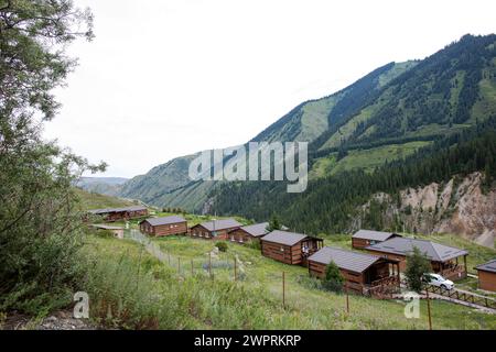 Traditionelles Kasachstans Jurtencamp im malerischen Bergtal in der Nähe des Flusses. Gemütliche Filz- und Holzjurten bieten lokale Gastfreundschaft inmitten von schneebedeckten Gipfeln. Stockfoto