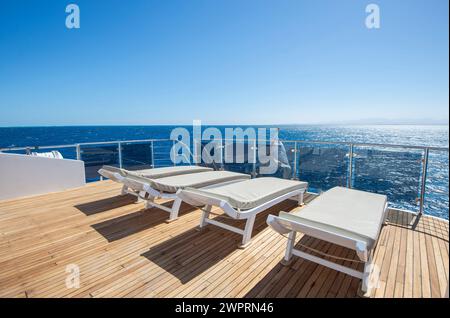 Teakholz-Sonnenterrasse einer großen Luxus-Motoryacht auf dem Meer mit Liegestühlen und einem tropischen Ozean Hintergrund Stockfoto