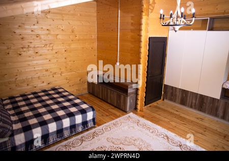 Das Schlafzimmer ist mit warmer Holztäfelung und einem weichen, einladenden Bett dekoriert. Ein schöner Kronleuchter sorgt für sanfte Beleuchtung. Stockfoto