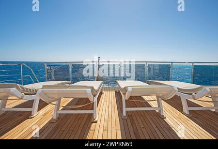 Teakholz-Sonnenterrasse einer großen Luxus-Motoryacht auf dem Meer mit Liegestühlen und einem tropischen Ozean Hintergrund Stockfoto