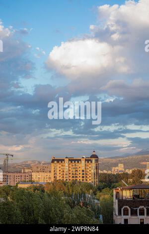 Eine atemberaubende Stadtlandschaft mit Bergen im Hintergrund, umgeben von grünen Bäumen unter einem blauen Himmel mit weißen Wolken. Stockfoto