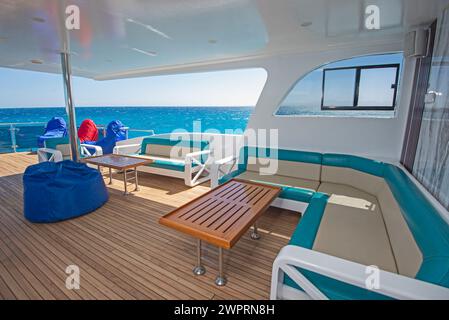 Sonnenterrasse aus Teakholz mit Holzdach einer großen Luxus-Motoryacht mit Stühlen, Sofabett und tropischem Meerblick im Hintergrund Stockfoto