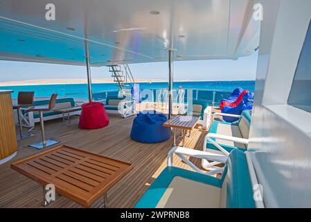 Sonnenterrasse aus Teakholz mit Holzdach einer großen Luxus-Motoryacht mit Stühlen, Sofabett und tropischem Meerblick im Hintergrund Stockfoto