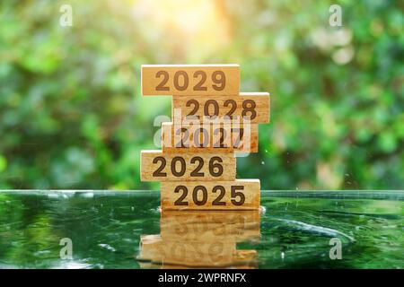 Stapel Holzblöcke mit den Jahren 2025 bis 2029 auf Wasserreflexionstisch mit Bokeh-Hintergrund Stockfoto
