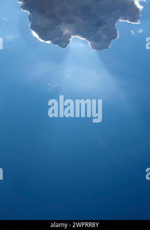 Hellblauer Himmel mit einer markanten Wolke, die durch Sonnenlicht beleuchtet wird Stockfoto