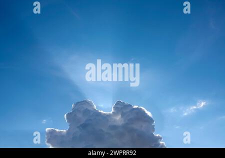 Hellblauer Himmel mit einer markanten Wolke, die durch Sonnenlicht beleuchtet wird Stockfoto