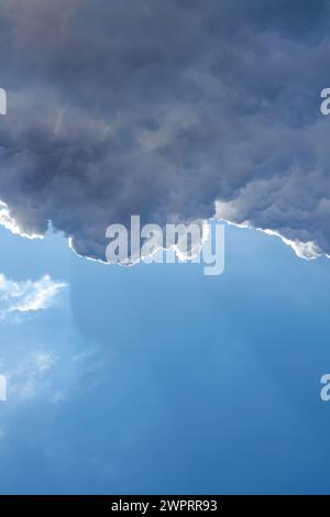 Hellblauer Himmel mit einer markanten Wolke, die durch Sonnenlicht beleuchtet wird Stockfoto