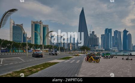 Doha Skyline in Doha, Katar von der Corniche Promenade am frühen Morgen mit Wagen und Elektrofahrrädern Stockfoto