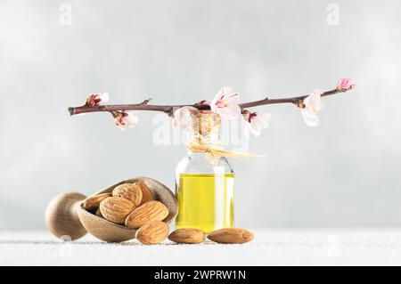 Glasflasche Mandelöl und Mandelnüsse, Mandeln mit Mandelblüten auf dem Tisch. Mandelhintergrundkonzept mit Kopierraum Stockfoto