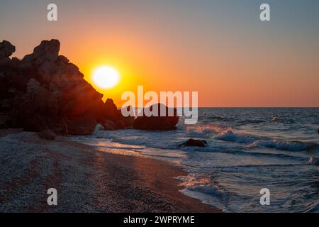 Wunderschöner Sonnenuntergang in einer felsigen Meeresbucht an einem Sommertag. Die Sonne blickt hinter dem Berg mit Strahlen hervor. Reisen und Tourismus. Stockfoto