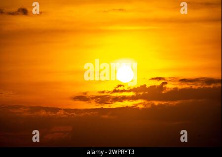 Feuriger Sonnenuntergang über dem Ozean, mit leuchtenden Orange- und Rottönen am Himmel. Die Sonne geht dramatisch unter, wirft warmes Licht auf dunkles Wasser unter und erzeugt B Stockfoto