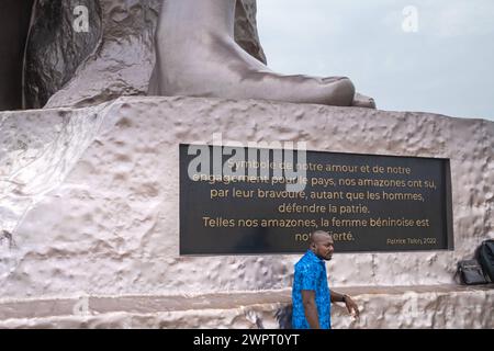 Monument Amazone Benin, Cotonou März 2024: Seit mitte 2022 steht das neue 30 Meter hohe Wahrzeichen der westafrikanischen Staat Benin. Die Amazone soll an die historische, rein weibliche Militäreinheit der Agojie auch Dahomey-Amazonen erinnern. Ein Mann posiert für ein Foto am Fusse der Statur. Auf die Tafel zu lesen: Symbole de notre amour et de notre Engagement pour le Pays, nos amazones ont su, par leur bravoure, autant que les hommes, dÃ fendre la patrie. Telles nos amazones, la femme BÃ ninoise EST notre fiertÃ . Patrice Talon, 2022 Google übersetzung: Als Symbol unserer Liebe und unseres Stockfoto