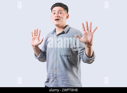 Verängstigter Mann mit erhobenen Händen isoliert. Junger Mann mit verängstigtem Gesicht und erhobenen Händen. Verängstigter und entsetzlicher Kerl mit erhöhten Palmen Stockfoto