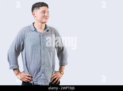 Zufriedener junger Mann mit Händen an der Hüfte, der zur Seite blickt. Junger Mann mit Händen auf Hüften, der sich eine Werbung an der Seite ansieht Stockfoto