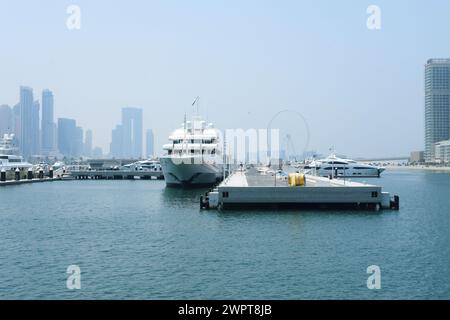 Luxusyachten, die an einem Jachthafen mit der trüben Skyline von Dubai und einem Riesenrad in der Ferne vor Anker liegen. Dubai, VAE - 15. August 2023 Stockfoto