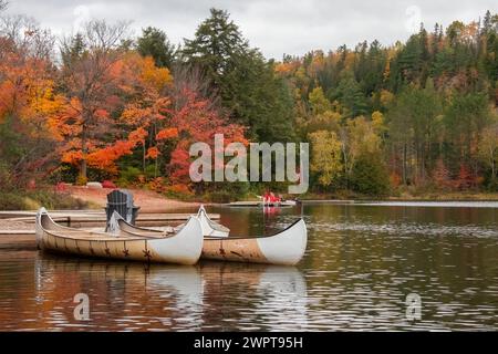 Zwei Kanus auf einem kleinen See in Ontario Kanada, während die Herbstfarben auf den Bäumen durch rot-orange und gelb im Hintergrund und rote Stühle kommen Stockfoto