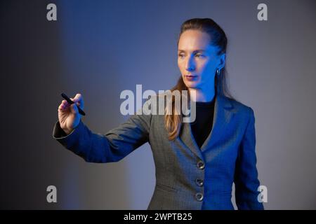 Geschäftsfrau, die einen hellen Bleistift in der rechten Hand auf grauem Hintergrund hält. Konzentrieren Sie sich auf die Hand. Blaue Farbkorrektur. Stockfoto