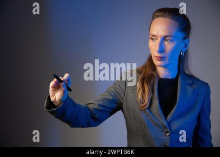 Geschäftsfrau, die einen hellen Bleistift in der rechten Hand auf grauem Hintergrund hält. Konzentrieren Sie sich auf die Hand. Nahaufnahme. Blaue Farbkorrektur. Stockfoto