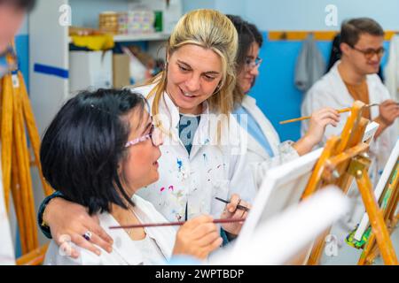 Lehrer, der eine behinderte Frau während des Malkurses mit anderen Menschen ermutigt Stockfoto