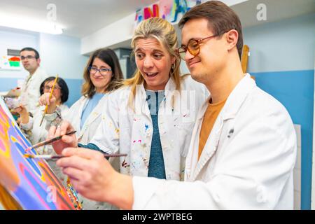 Der Lehrer hilft einem Mann mit Down-Syndrom, auf Leinwand zu malen in einem Malkurs Stockfoto