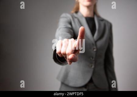 Porträt einer Geschäftsfrau mit ausgestrecktem Arm und Zeigefinger ohne Gesicht. Grauer Hintergrund. Stockfoto