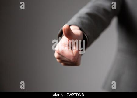 Die Hand einer Geschäftsfrau, deren Arm nach vorne gestreckt ist, in einer Geste mit geballter Faust und Daumen nach oben, was bedeutet, dass alles gut ist. Grauer Hintergrund. Stockfoto