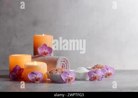 Meersalz, Handtücher, Orchideenblüten und brennende Kerzen auf grauem Hintergrund. Spa-Konzept mit Kopierraum. Stockfoto