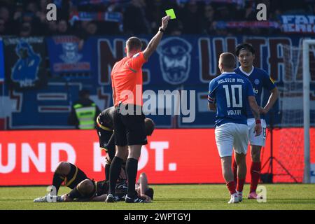 Kiel, Deutschland. März 2024. Fußball: Bundesliga 2, Holstein Kiel - Karlsruher SC, Spieltag 25, Holstein Stadium. Schiedsrichter Florian Exner (M) zeigt Kiels Lewis Holtby nach einem Foul die gelbe Karte. Hinweis: Gregor Fischer/dpa – WICHTIGER HINWEIS: gemäß den Vorschriften der DFL Deutscher Fußball-Liga und des DFB Deutscher Fußball-Bundes ist es verboten, im Stadion und/oder des Spiels aufgenommene Fotografien in Form von sequenziellen Bildern und/oder videoähnlichen Fotoserien zu verwenden oder zu nutzen./dpa/Alamy Live News Stockfoto