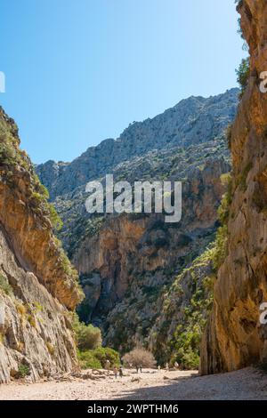 Torrent de Pareis, Wanderer spazieren durch eine sonnenverwöhnte Schlucht eines ausgetrockneten Flusses in den Bergen mit Felsbrocken und Kieselsteinen zwischen hohen, steilen Felsen Stockfoto