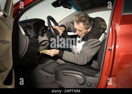 Ein älterer Mann kümmert sich um die Reinigung des Innenraums des Autos auf dem Naturparkplatz Stockfoto