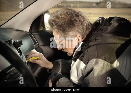 Ein älterer Mann kümmert sich um die Reinigung des Innenraums des Autos auf dem Naturparkplatz Stockfoto