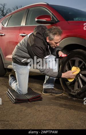 Ein älterer Mann kümmert sich um die Reinigung des Autos im Freien auf dem Naturparkplatz Stockfoto