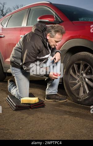 Ein älterer Mann kümmert sich um die Reinigung des Autos im Freien auf dem Naturparkplatz Stockfoto