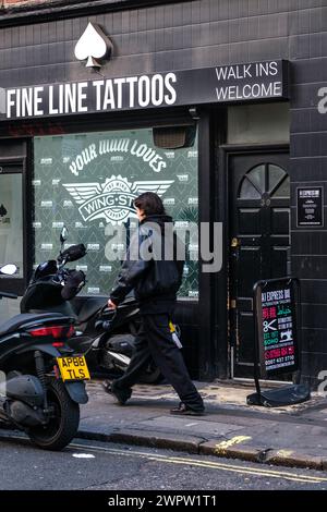 Soho, London, Großbritannien, 08. März 2024, Mann, der an Fine Line Tattoo Shop vorbeiläuft und Motorroller draußen parkt Stockfoto