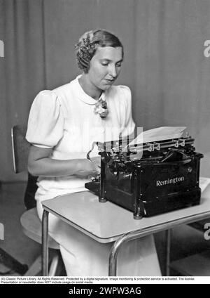 Büromädchen in den 1930ern Eine junge Frau an einer Schreibmaschine. Sie ist hübsch gekleidet, mit ihren Haaren in einer typischen Frisur des Jahrzehnts. 1935 Stockfoto